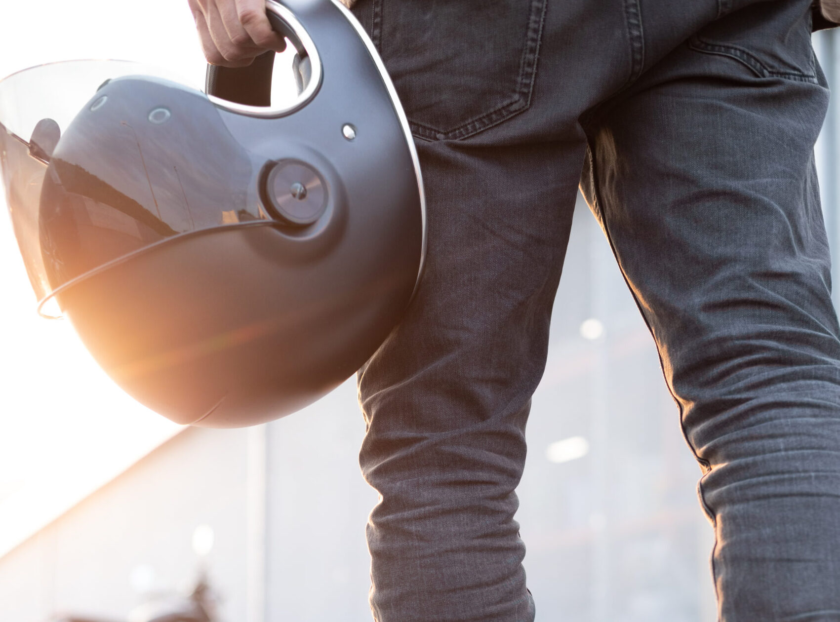 Close-up of a handsome rider biker guy hand with black helmet in front of classic style cafe racer motorcycle. Bike custom made in vintage garage. Brutal fun urban lifestyle. Outdoor portrait.